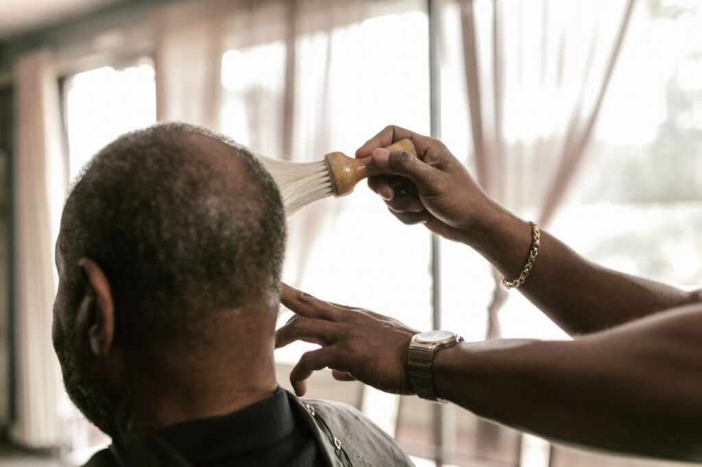 Close-up of a barber using a brush to dust client's head in a barbershop setting.